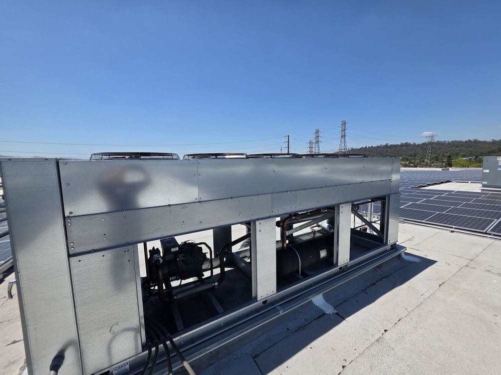 Rooftop HVAC unit with vents on a flat industrial roof under a clear blue sky.
