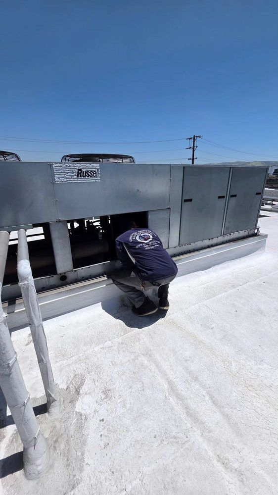 Person crouching beside gray rooftop HVAC unit under clear blue sky