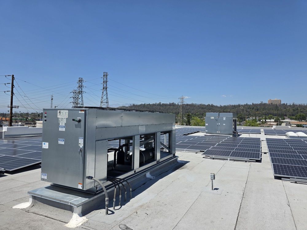 Rooftop solar panels beside gray HVAC units under a clear blue sky