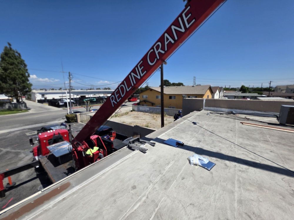Red Line Crane lifting materials onto a flat roof near workers on a construction site