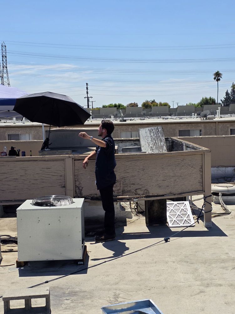 Person on a rooftop adjusting a black umbrella beside rooftop equipment under a clear sky