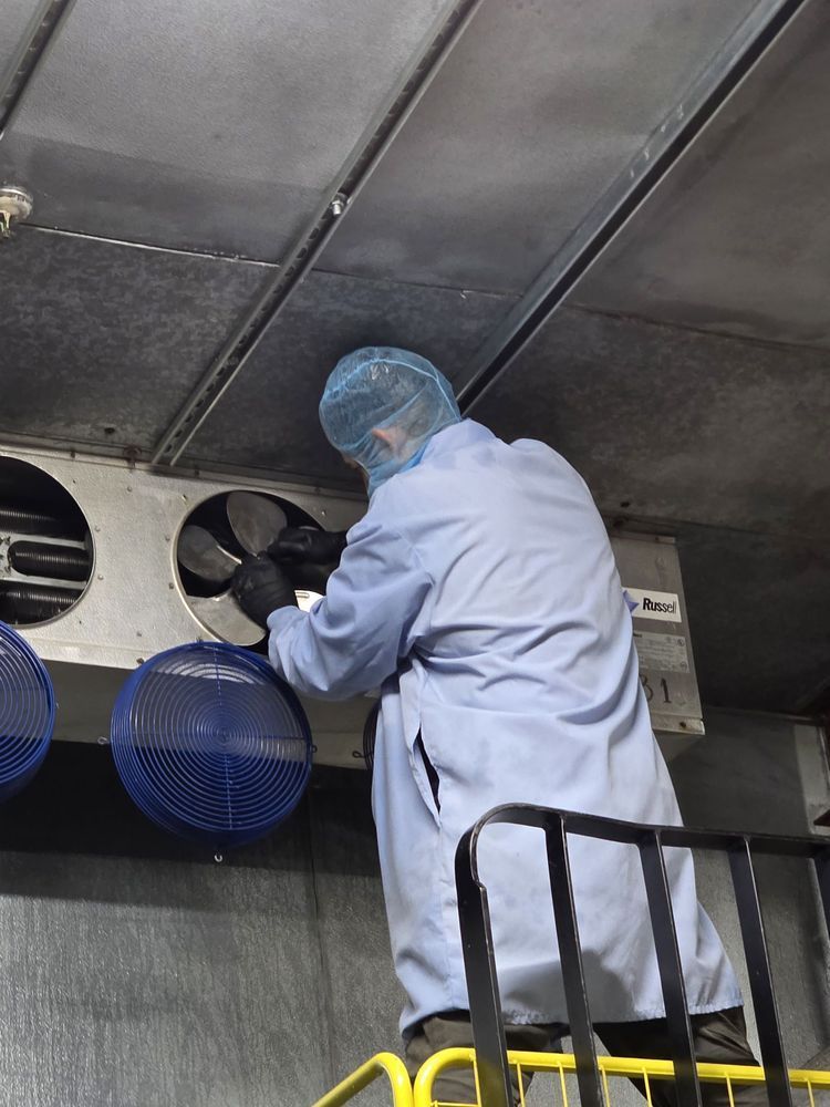 Worker in a lab coat inspecting large industrial fans inside a metal chamber