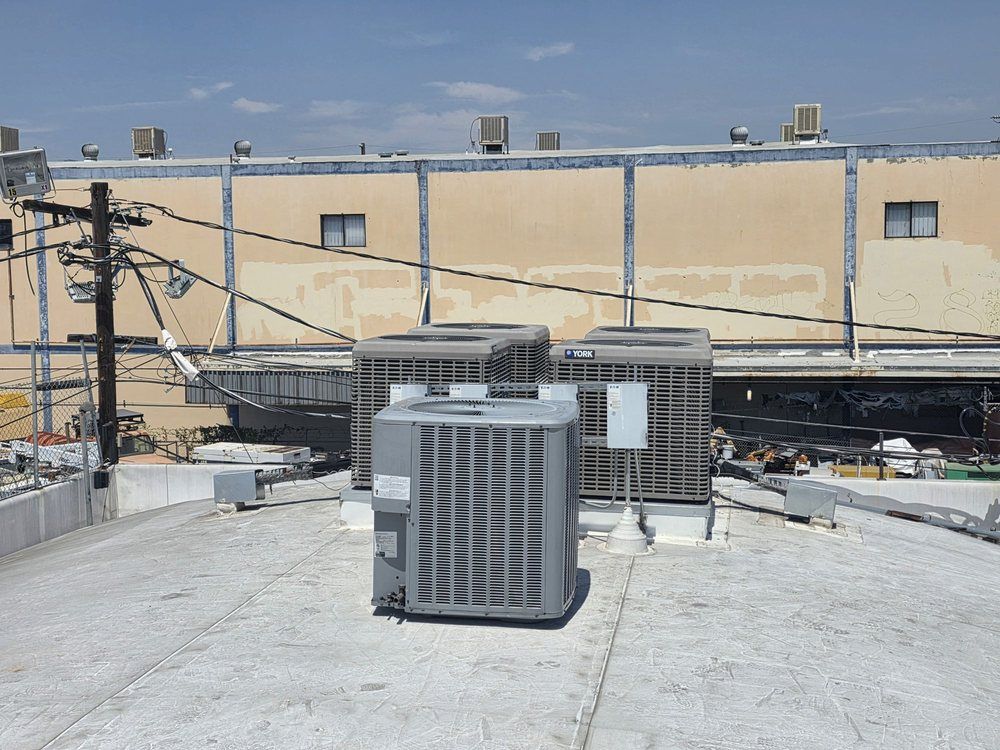 Rooftop HVAC units and utility lines in front of a beige industrial building.