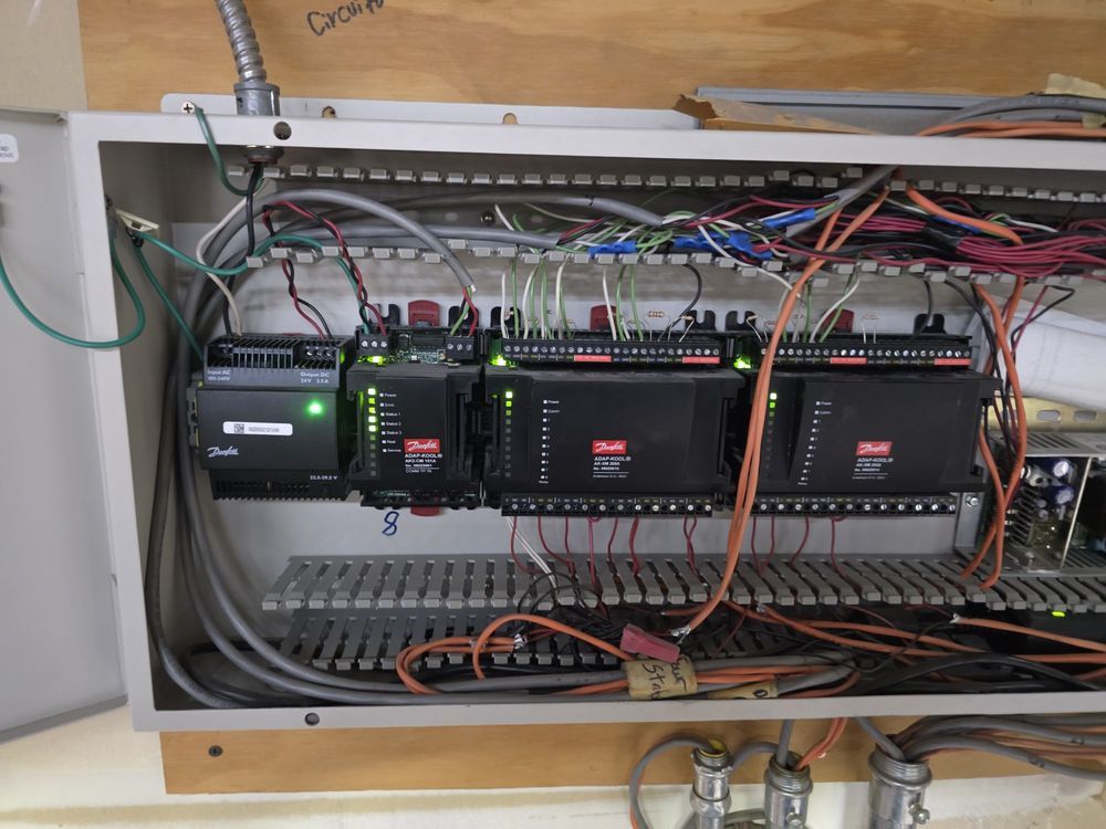 Open electrical control panel with wiring and circuit modules mounted inside a white cabinet