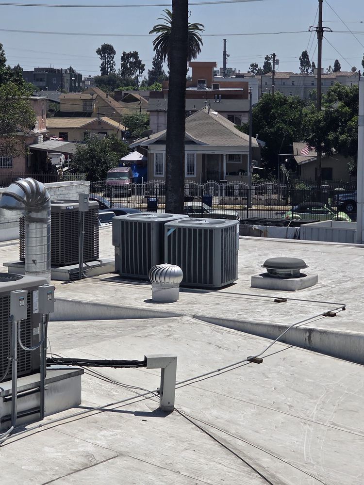 Rooftop with HVAC units, vents, and utility equipment in an urban neighborhood under a clear sky