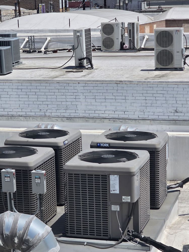 Rooftop with several outdoor HVAC units and air conditioners in front of a white brick parapet.