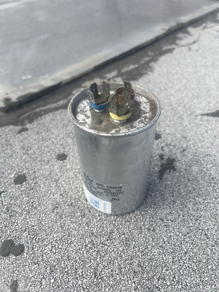 Metal cylindrical capacitor on a gray rooftop, with wires attached to the top.