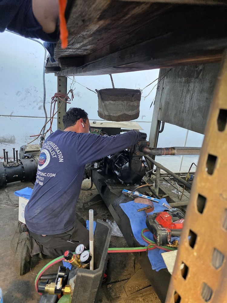 Technician working on machinery aboard a boat, with tools and equipment around him.