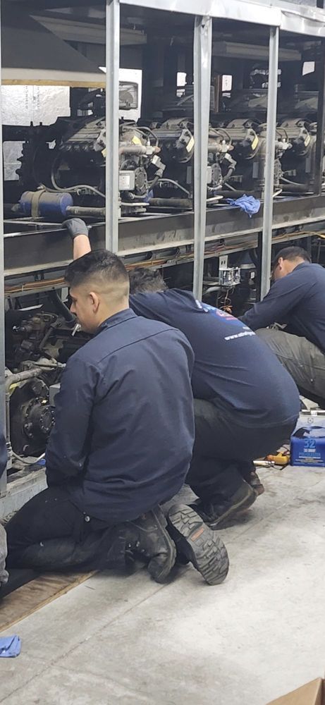 Workers in blue uniforms kneel beside a glass display case during maintenance or assembly.