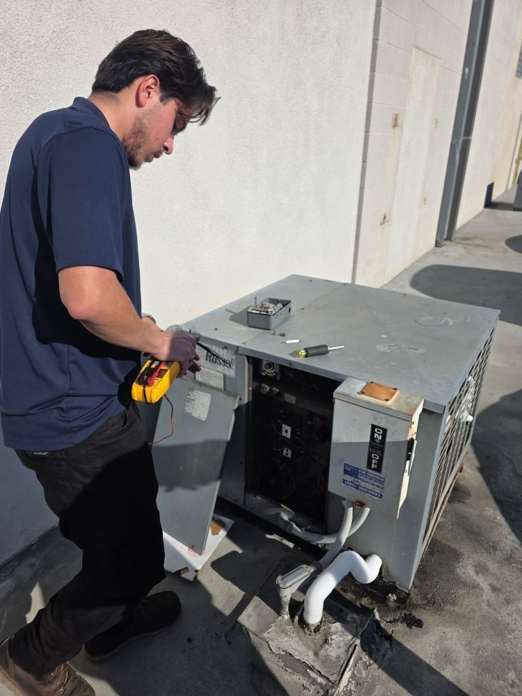 Man in navy shirt installing a metal appliance or cabinet outdoors with tools beside him