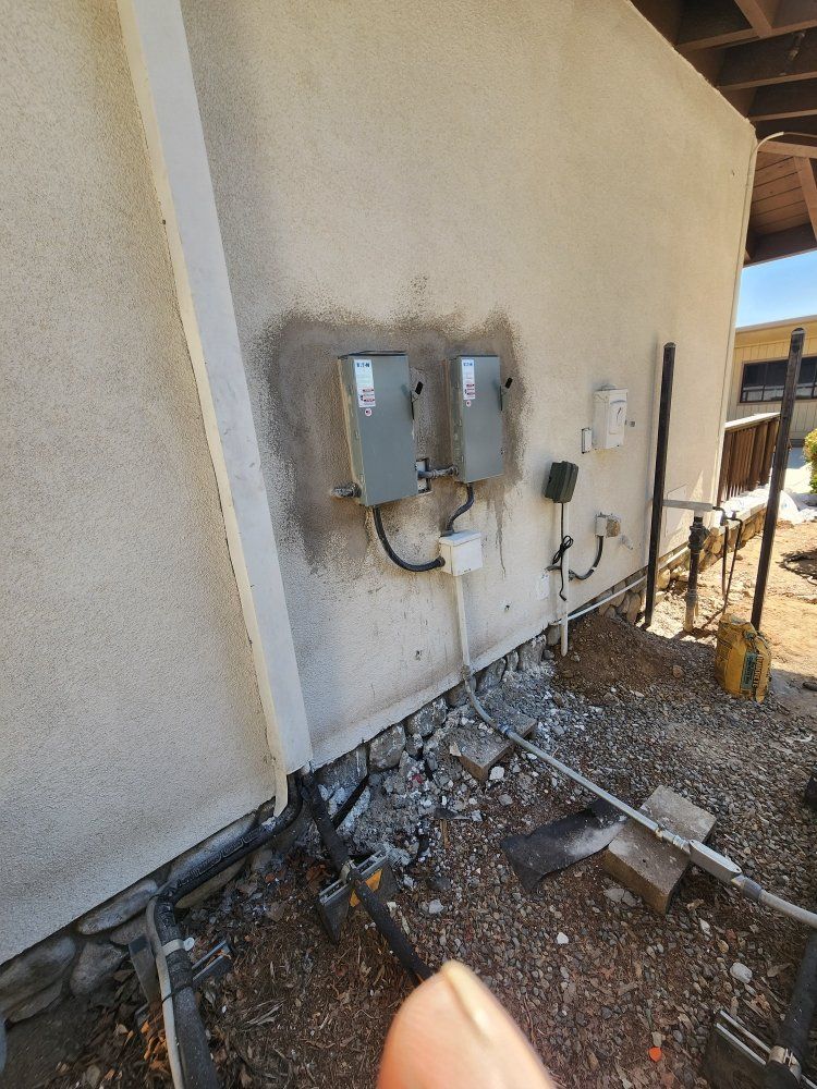 Utility meters and electrical boxes mounted on an exterior stucco wall with debris on the ground.