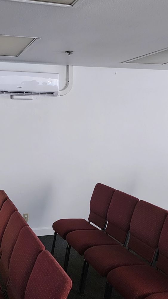 Rows of maroon chairs in a sparse waiting room with a wall-mounted air conditioner above.