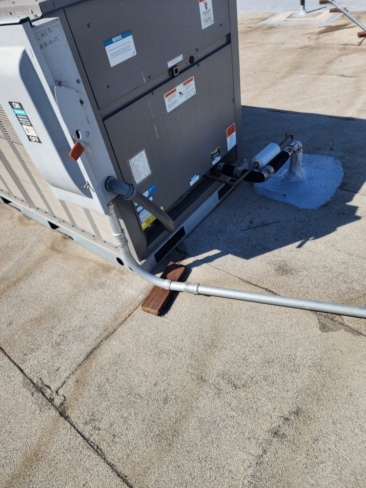 Outdoor HVAC unit with bent conduit and a blue tarp covering debris on a concrete pad