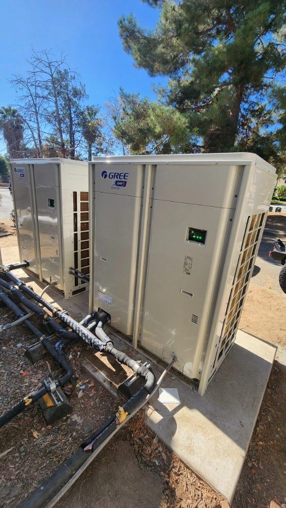 Outdoor HVAC equipment and metal piping beside a building, with white utility units on a concrete pad.