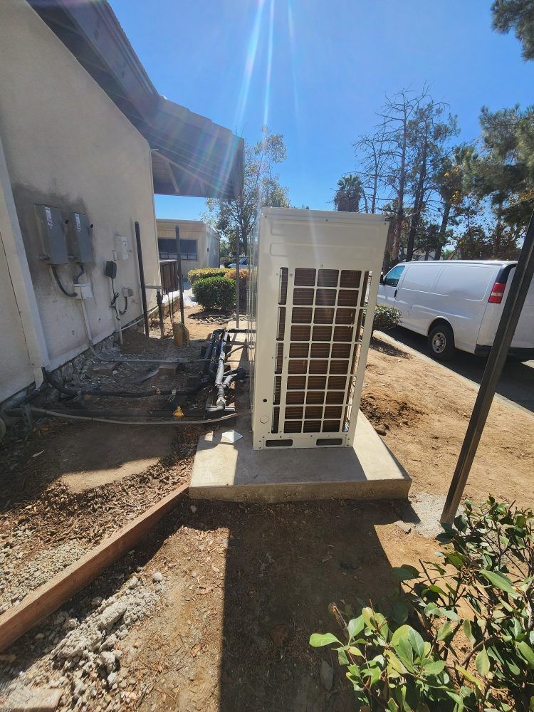 Outdoor HVAC unit beside a building, with a white van parked nearby on a sunny day