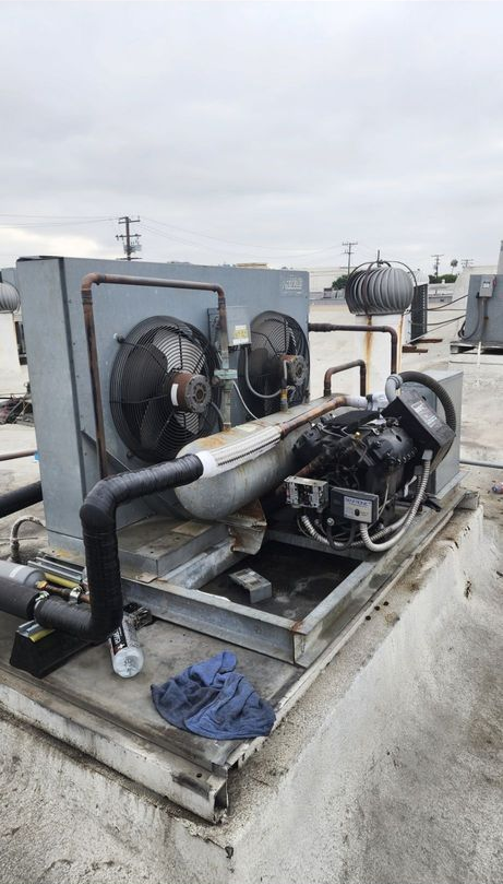 Industrial rooftop HVAC unit with fans, ducts, and pipes on a concrete platform under a cloudy sky