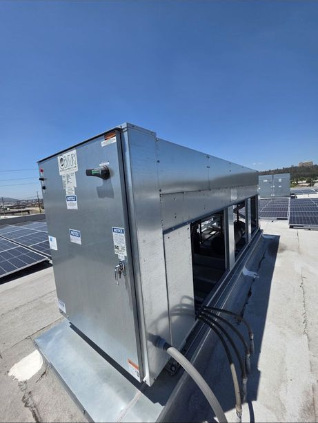 Metal rooftop HVAC unit with black cables against a clear blue sky