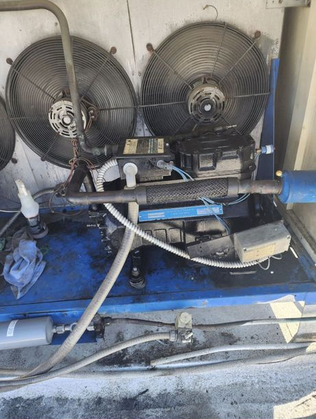 Industrial machine with two black fans, blue base, and hoses in a utility room