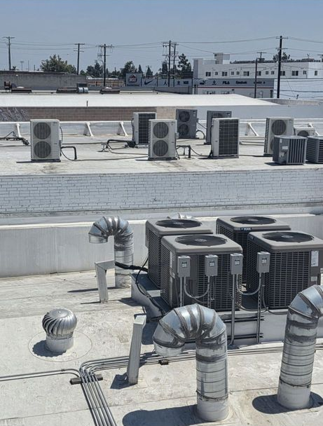 Rooftop HVAC units and ventilation pipes on a flat commercial roof under a clear sky