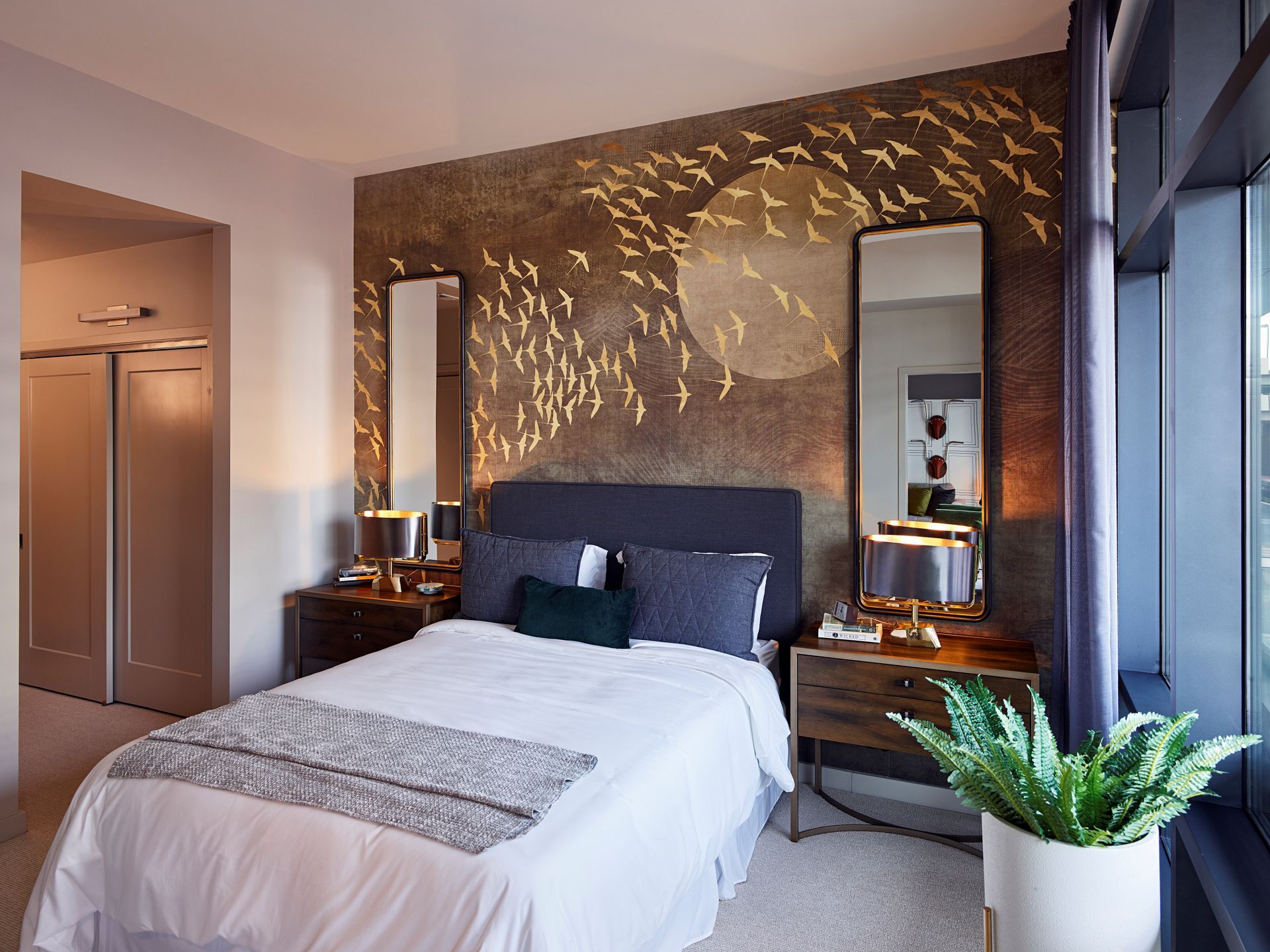 A bedroom with a large bed, two nightstands, a mirror, and a plant at Solaire 8250 Georgia in Silver Spring, MD.