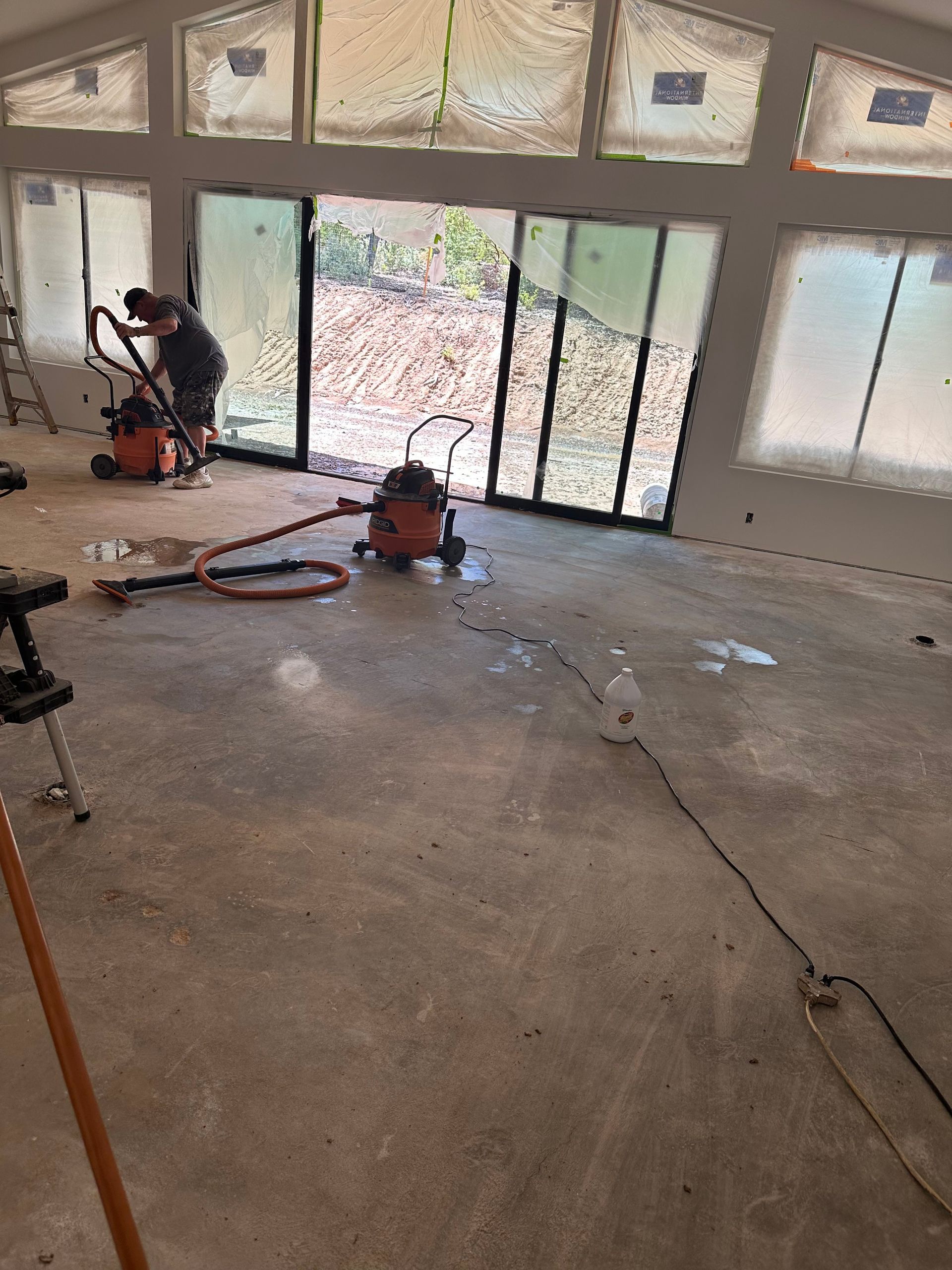 Indoor construction area with concrete floor, large windows, and tools/equipment near the wall