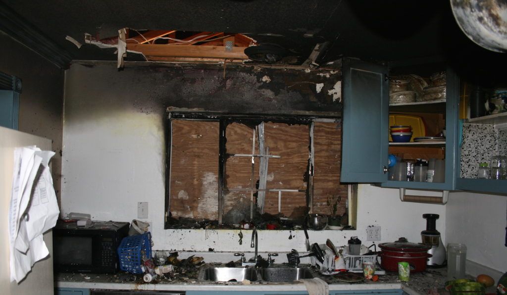 Damaged kitchen with burned ceiling, broken window, and debris around the sink and counters