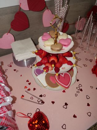Valentine-themed dessert table with heart decorations, strawberries, and pink-white sweets on tiered trays