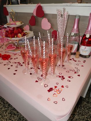 Pink party table with heart decorations, champagne flutes, strawberries, and bottles of sparkling drink