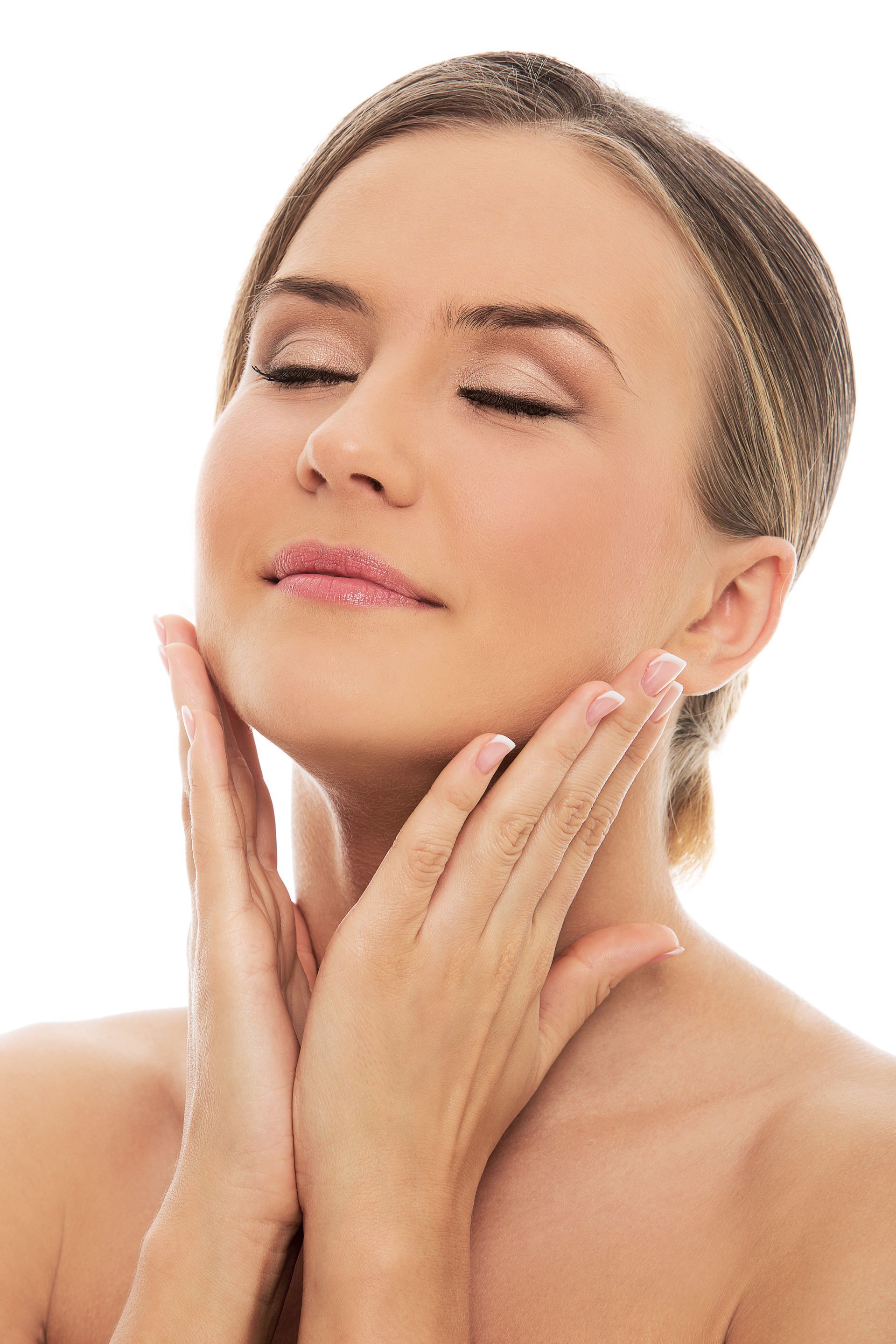 Woman with eyes closed gently applying skincare to her face on a white background
