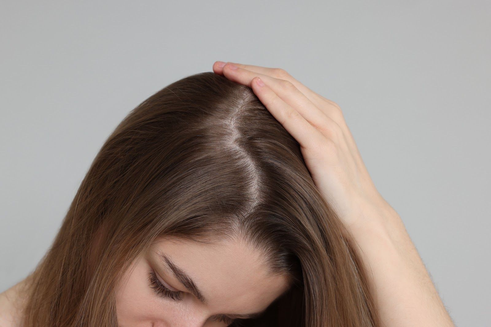 Woman holding her head with one hand, looking down against a plain gray background