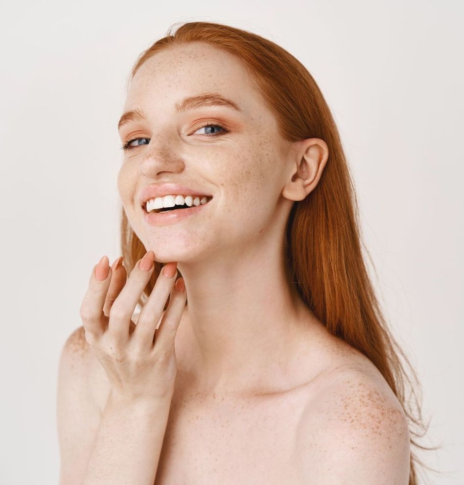 Smiling red-haired person touching their chin against a white background