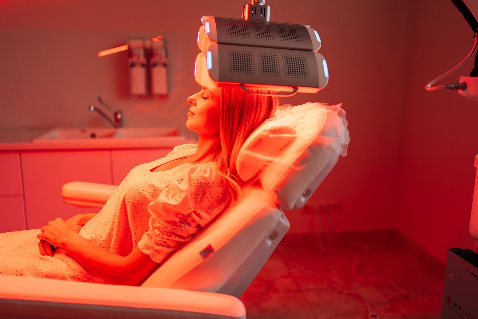 Person reclining in a red-lit medical chair with a device mounted above the head