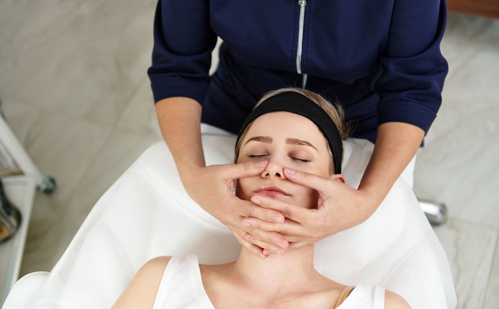 Facial massage in progress on a woman lying on a treatment bed with eyes closed