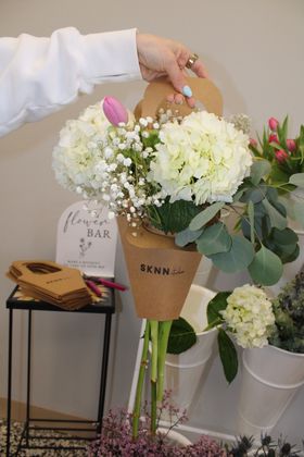 Hand holding a brown paper bouquet of white flowers and pink tulips in a softly lit room