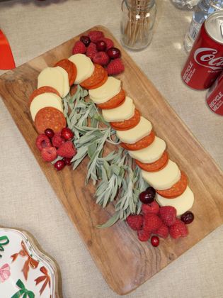 Gourmet charcuterie board with sliced cheese, herbs, berries, and crackers on a wooden tray beside soda cans