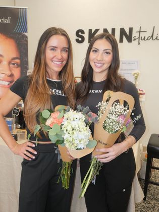 Two women holding flowers and a gift basket at a SKIN studio event booth