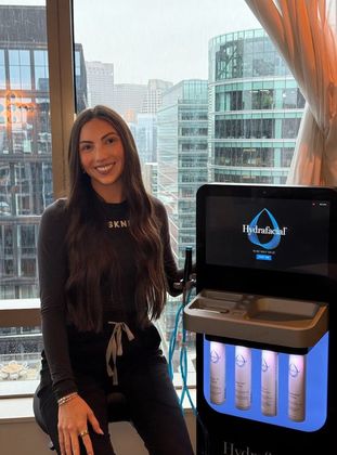 Woman posing beside a water dispenser in a high-rise room with city skyline in the background