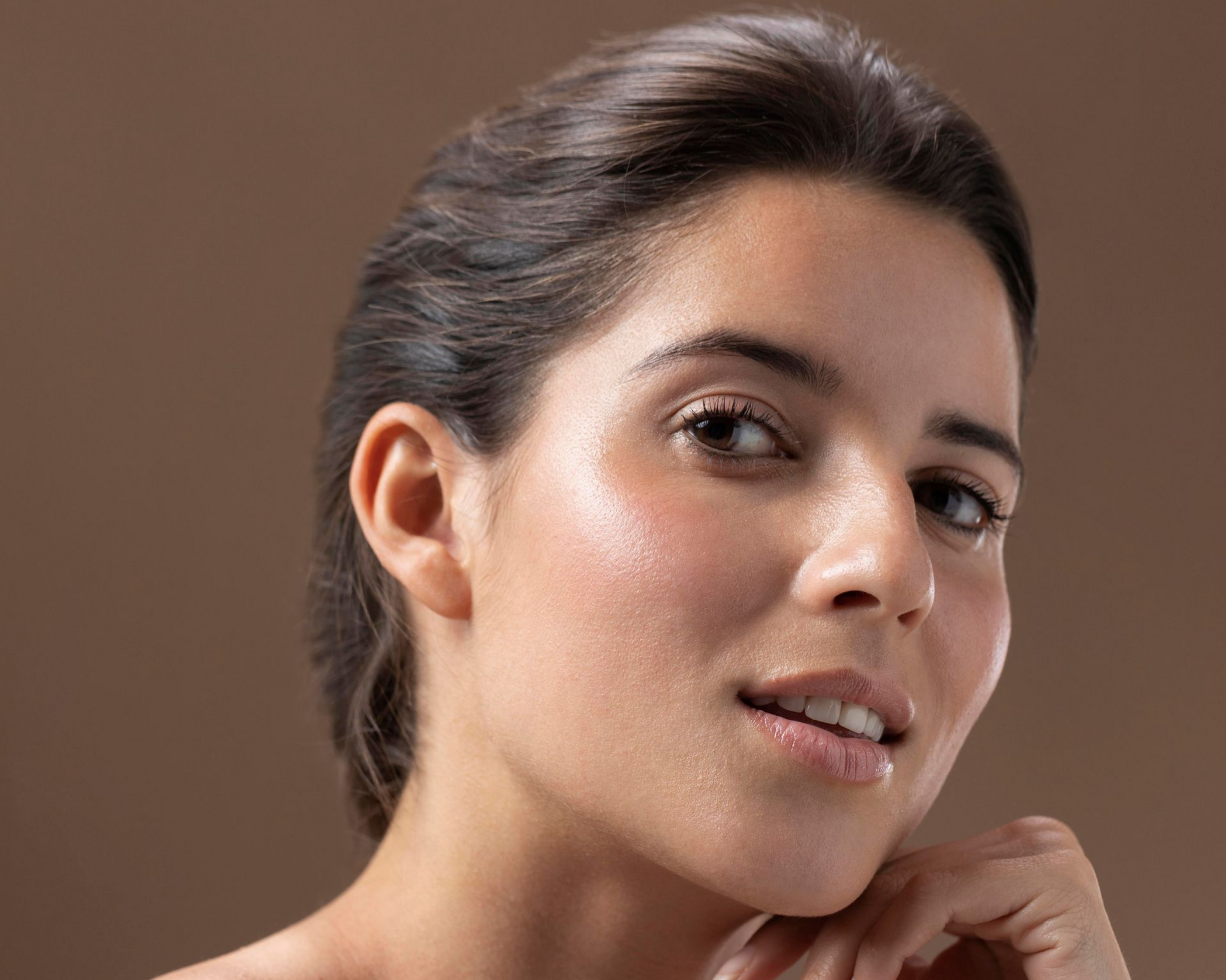 Close-up portrait of a smiling woman with dark hair against a plain brown background