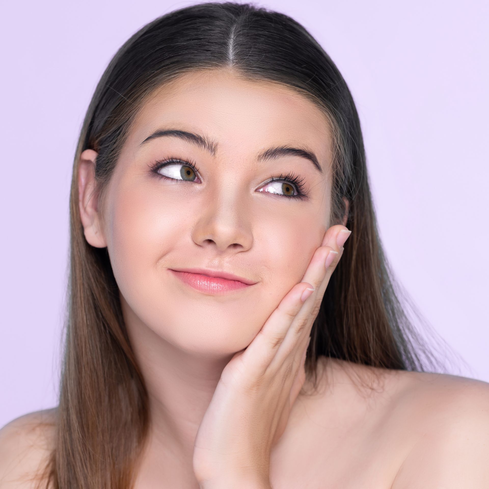 Smiling woman with dark hair touching her cheek against a light purple background