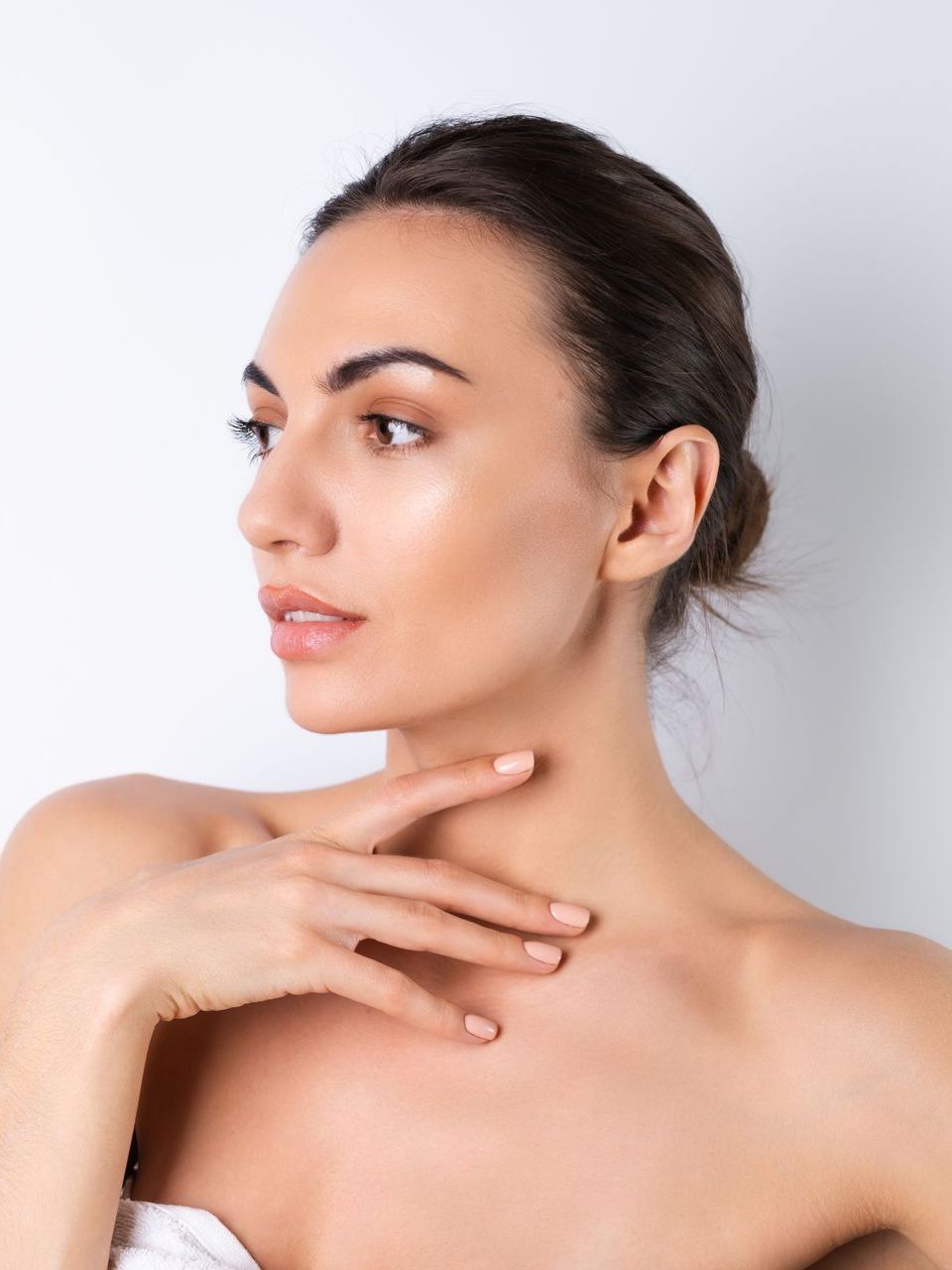 Woman with bare shoulders touching her neck, looking to the side against a plain light background