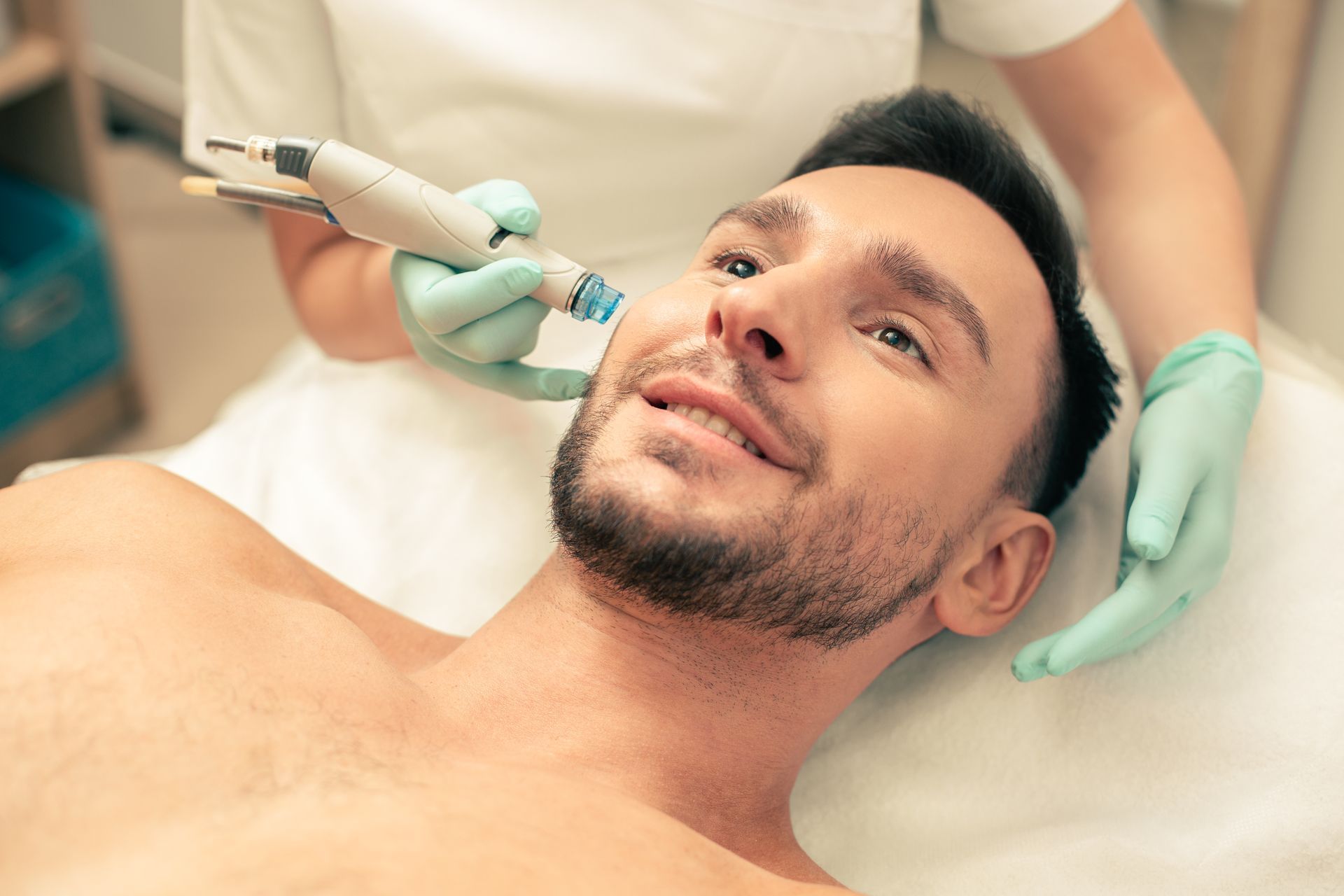 Cosmetic facial treatment with a handheld device on a reclining man in a clinic