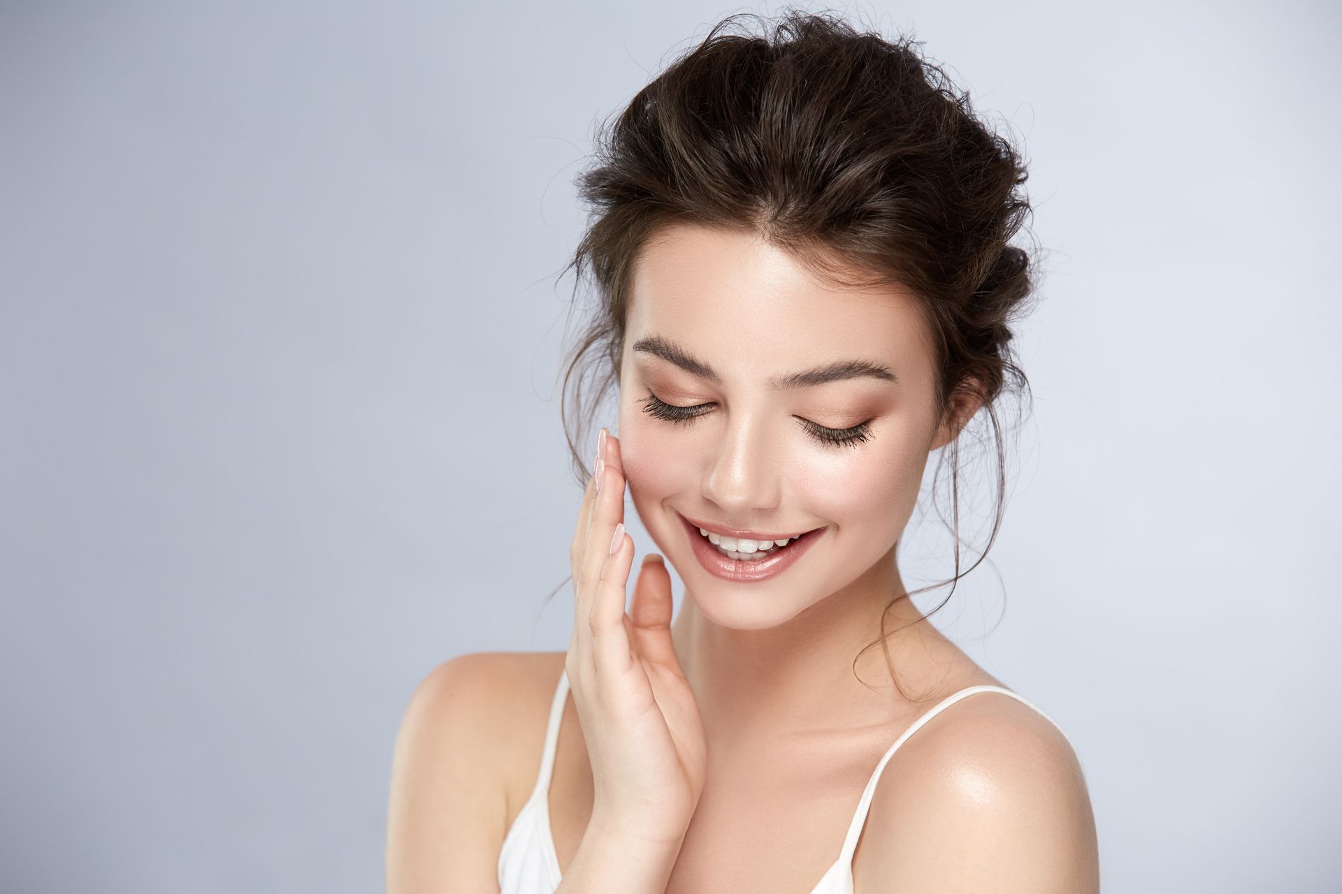Smiling woman gently touching her cheek against a light gray background