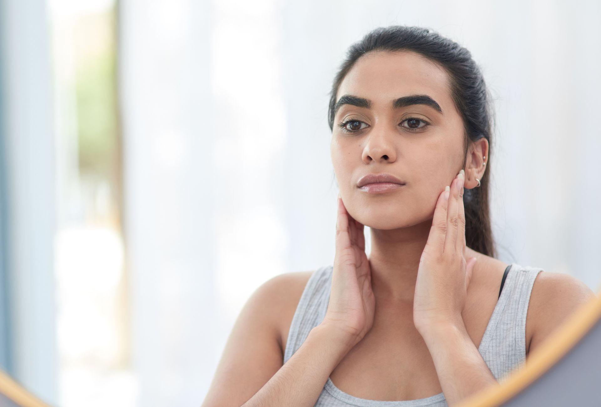 Person applying skincare to face in a bright bathroom mirror.