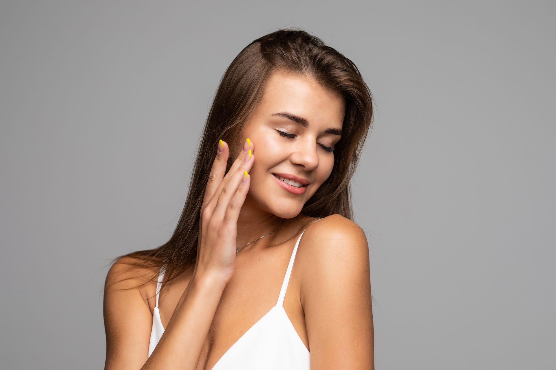 Smiling woman touching her cheek with yellow lotion on a gray background