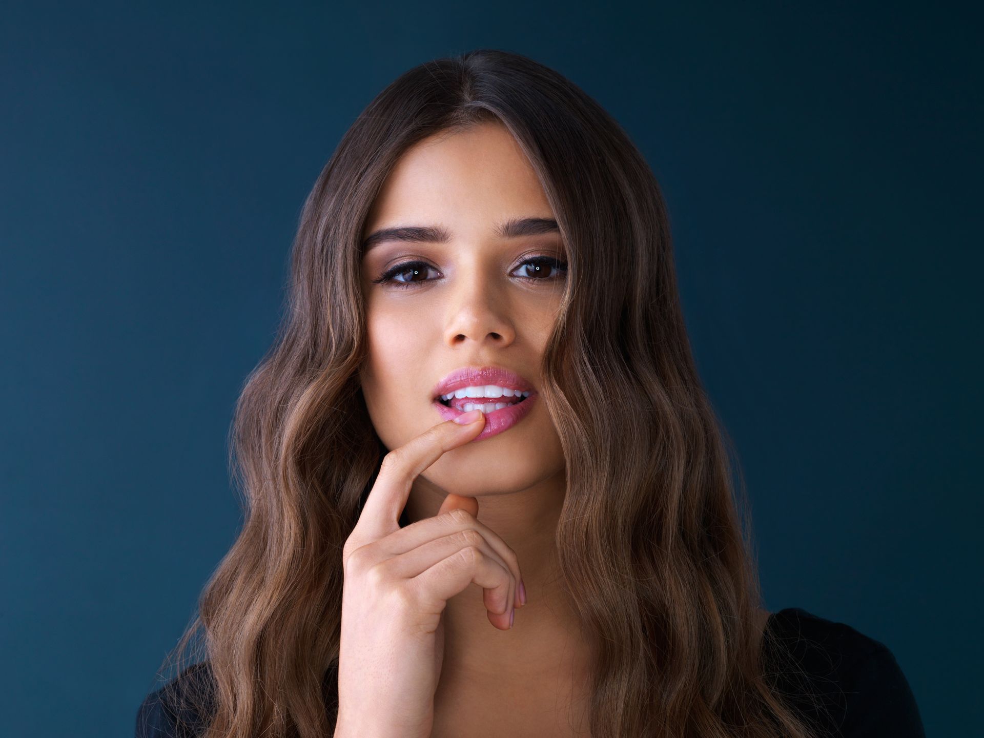 Woman with long brown hair touching her lip against a dark blue background