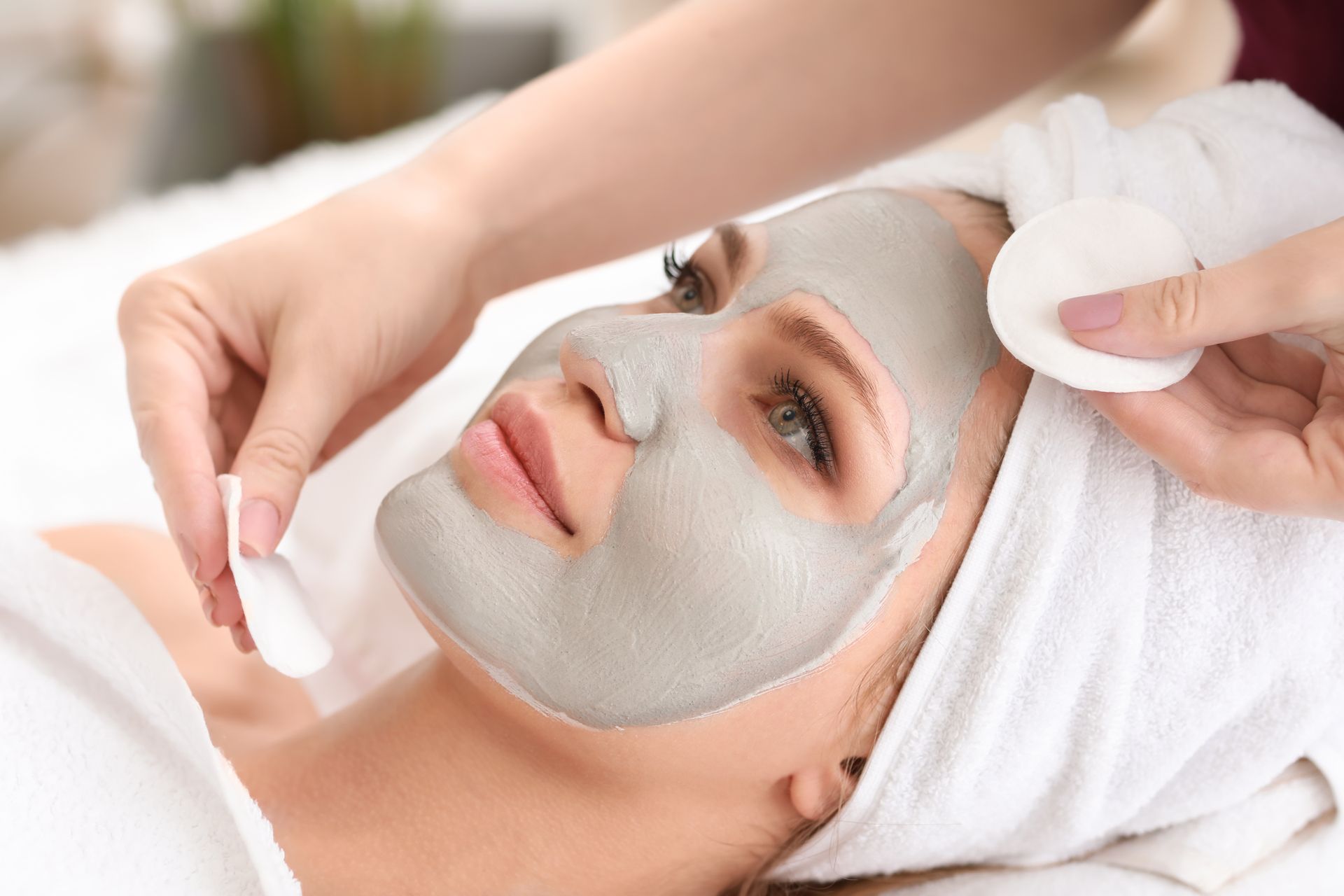 Facial mask being applied to a woman lying down with a towel wrapped around her head