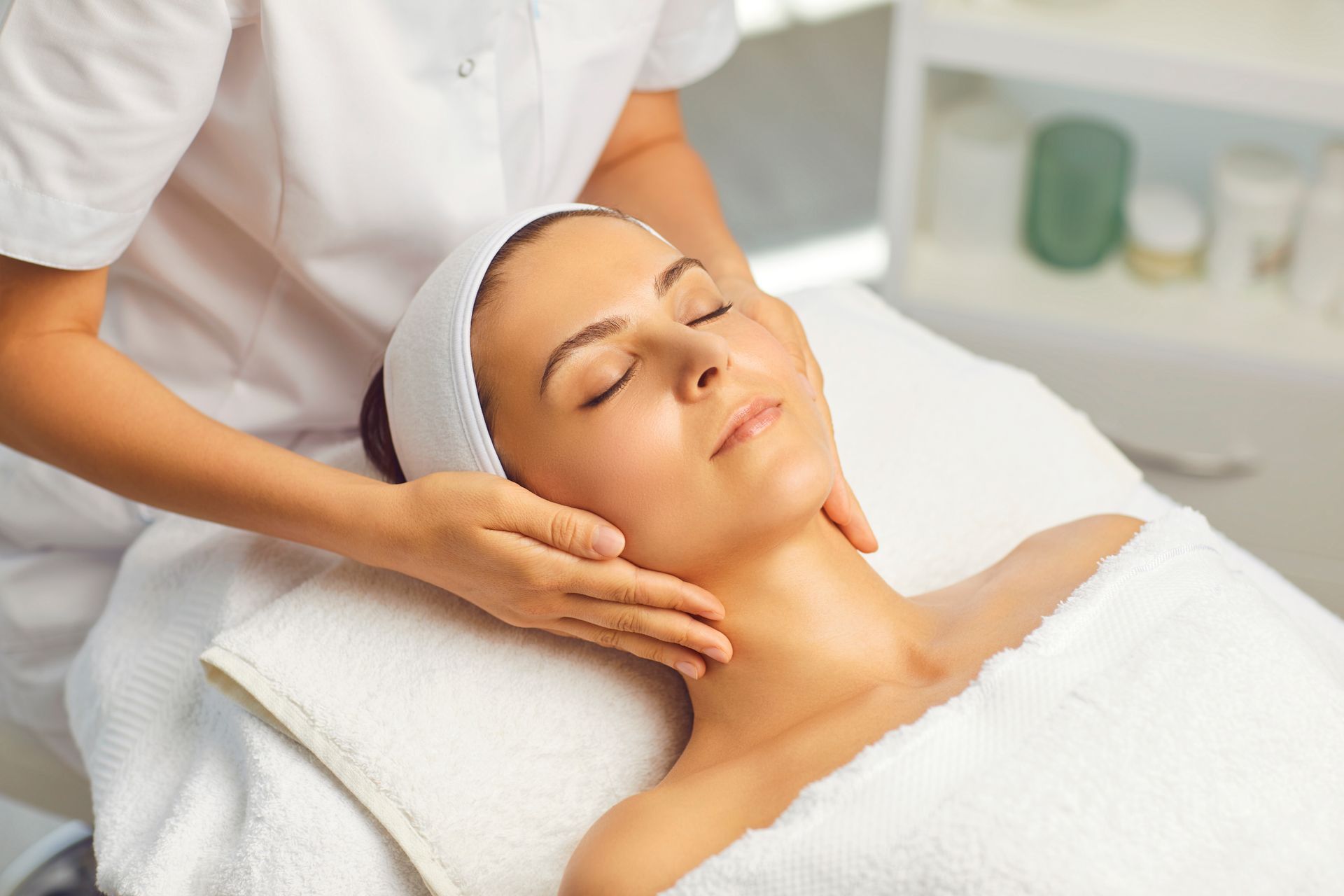 Spa therapist giving a facial massage to a relaxed client lying on a treatment bed