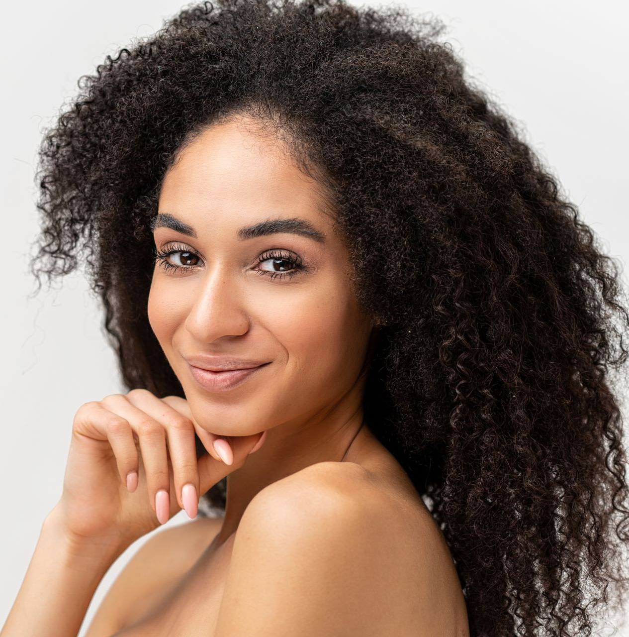 Smiling woman with curly dark hair resting her chin on her hand against a light background