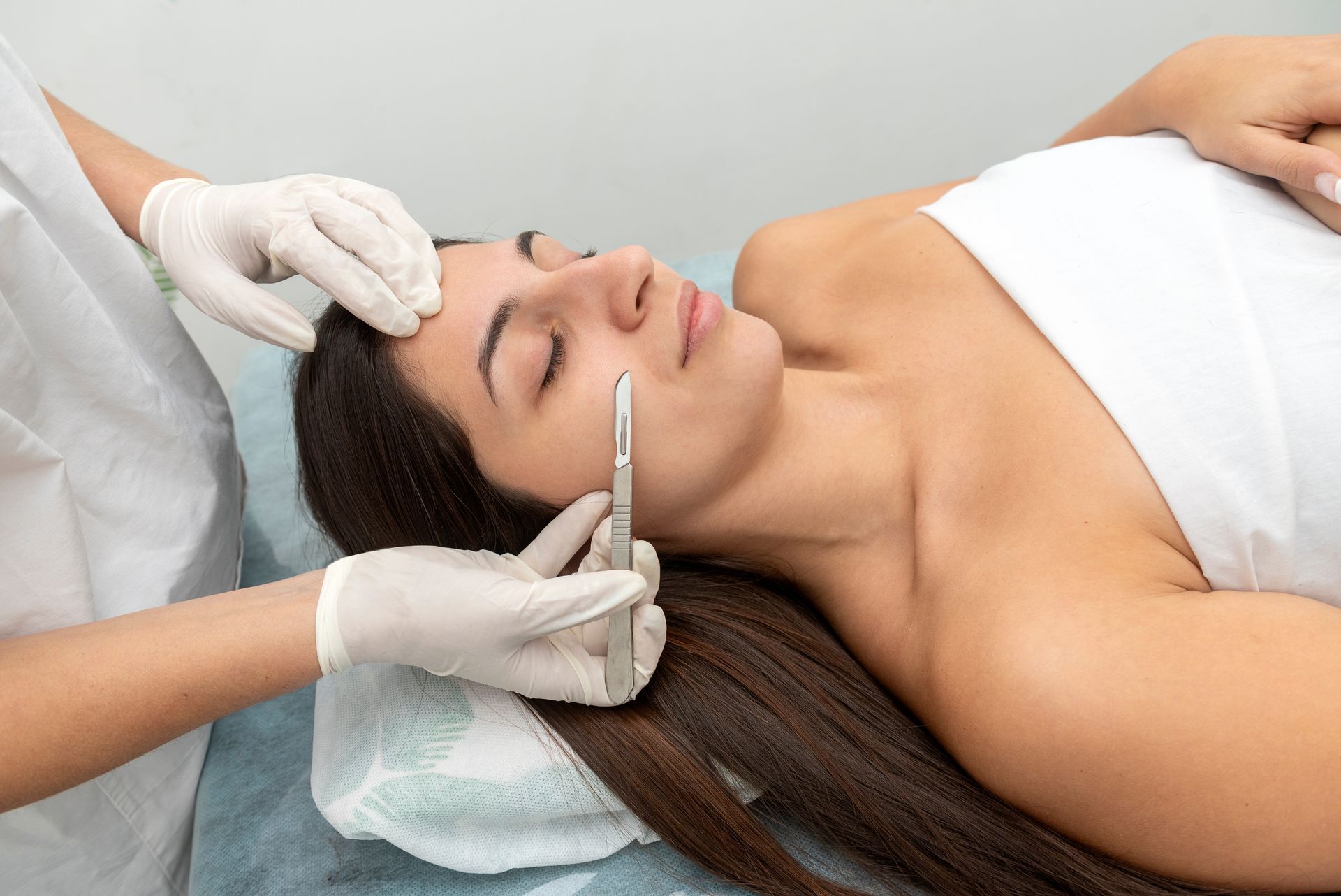 Cosmetic treatment on a woman’s face with a handheld device while lying on a treatment bed