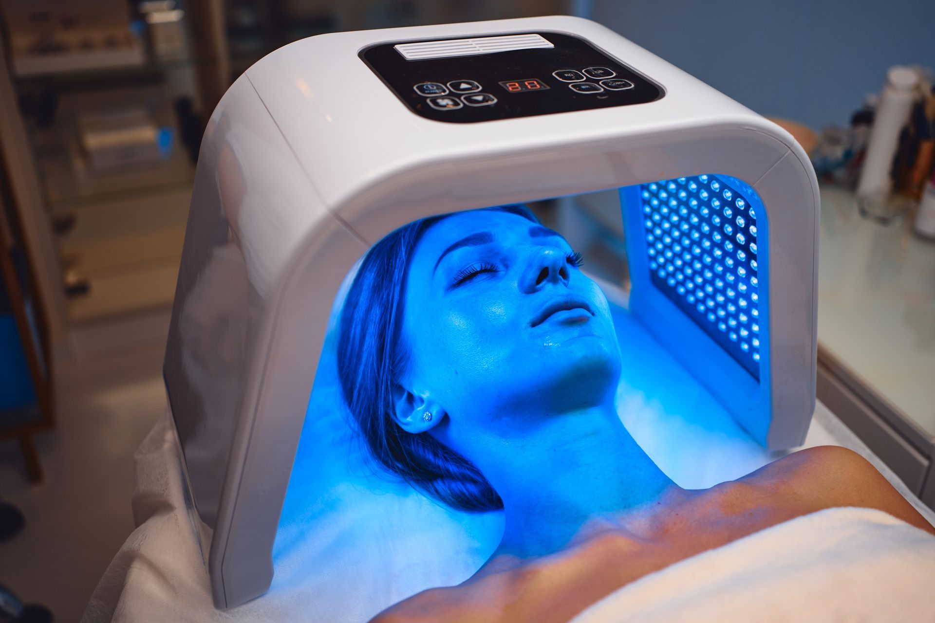Woman under blue LED light therapy device on a treatment table